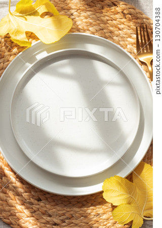 Table Setting with Yellow Leaves on White Plate and Woven Placemat under Sun Light Table Setting with Yellow Leaves on White Plate and Woven Placemat under Sun Light 130704388