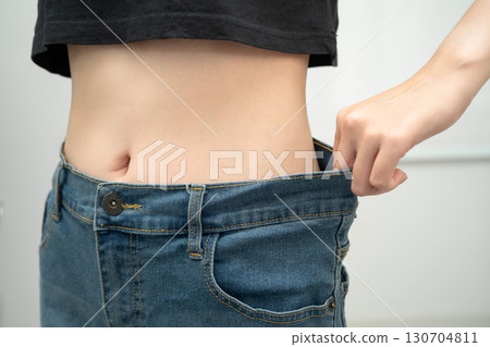 Young Asian woman losing weight wearing loose pants in oversize jeans. Young Asian woman losing weight wearing loose pants in oversize jeans. 130704811