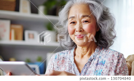 Older Asian woman holding a tablet answers survey questions in bright office corner. Survey research answer checklist 130704840