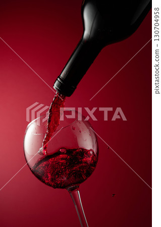 Pouring red wine from a bottle into a glass. Pouring red wine from a bottle into a glass. 130704958