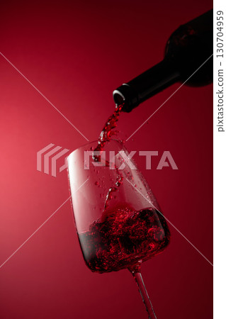 Pouring red wine from a bottle into a glass. 130704959