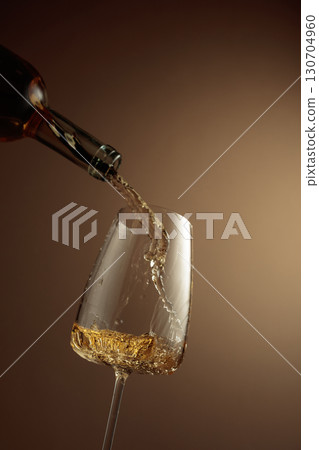 Pouring white wine from a bottle into a glass. Pouring white wine from a bottle into a glass. 130704960