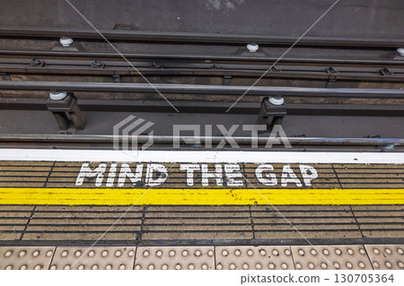 Mind the Gap Safety Warning on Subway Platform with Yellow Line and Rail Tracks 130705364