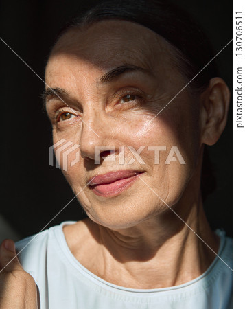 Mature woman with soft smile in sunlight highlighting natural skin texture 130706511