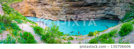 Turquoise mountain lake at the foot of a rocky cliff, surrounded by greenery and stones Turquoise mountain lake at the foot of a rocky cliff, surrounded by greenery and stones 130706606
