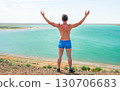 Man with raised arms stands by a turquoise lake, enjoying freedom 130706683