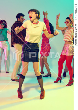 Happy young woman dancing confidently in front of retro styled group 130706711
