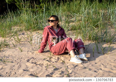 Woman and moody cat basking on sandy beach. Grumpy feline on owner lap distrusting new walking 130706783