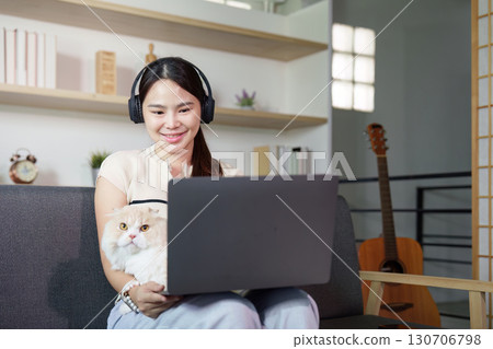 Remote Work with Cat. Young woman wearing headphones and working on laptop at home. 130706798