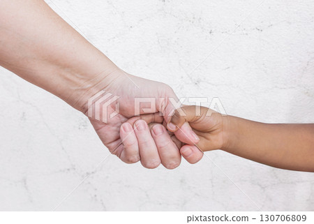 Hands of child and adult. Interracial family holding hands, Caucasian mother and dark skin son or daughter. Motherhood and childhood concept. Close-up a mother giving a hand to her child Hands of child and adult. Interracial family holding hands, Caucasian mother and dark skin son or daughter. Motherhood and childhood concept. Close-up a mother giving a hand to her child 130706809