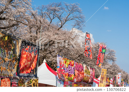 在櫻花節上，在藍天和櫻花的映襯下，五顏六色的旗幟排列在小吃攤上。 130706822