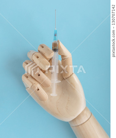 Wooden human hand with syringe with vaccine for disease on light blue background. Doctor holds syringe with medical injection. Health care and disease prevention concept. Vertical photo. 130707142