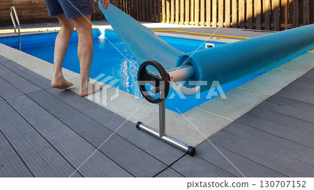 Man covers swimming pool with cover for protection against dirt, leaves, heating and cooling water. 130707152
