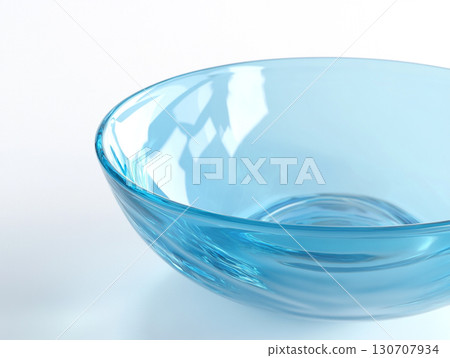 A close-up of a clear, light blue glass bowl on a white surface, showcasing its smooth, translucent surface and a subtle spiral pattern at its base. 130707934