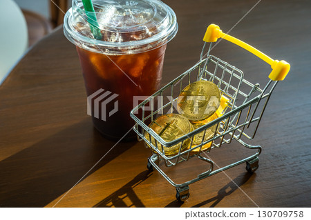 Close-up of Golden bitcoins or cryptocurrency coin or symbols in shopping cart and Americano iced coffee or black in white table. Future currency concept. 130709758