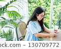 a portrait of beautiful happy asian woman traveler wearing a beautiful blue dress lifestyle enjoying holding using smartphone cellphone casual working in sitting coffee shop restaurant background 130709772