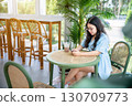 a portrait of beautiful happy asian woman traveler wearing a beautiful blue dress lifestyle enjoying holding using smartphone cellphone casual working in sitting coffee shop restaurant background 130709773