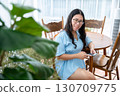 a portrait of beautiful happy asian woman traveler wearing a beautiful blue dress lifestyle enjoying holding using smartphone cellphone casual working in sitting coffee shop restaurant background 130709775