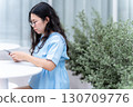 a portrait of beautiful happy asian woman traveler wearing a beautiful blue dress lifestyle enjoying holding using smartphone cellphone casual working in sitting coffee shop restaurant background 130709776