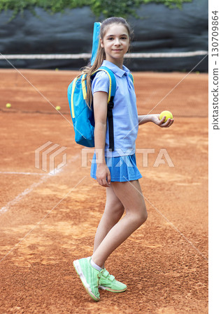 Young tennis player with blue outfit on clay court holding racket and ball 130709864