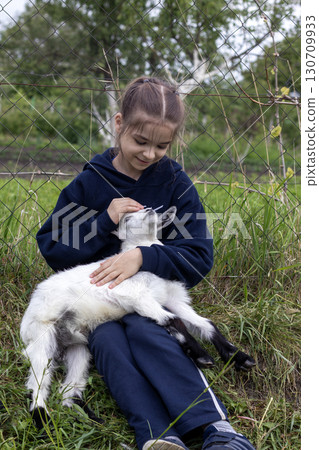 Young girl holding and petting a white baby goat outdoors 130709933