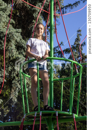 Girl standing on a green play structure surrounded by trees outdoors Girl standing on a green play structure surrounded by trees outdoors 130709950
