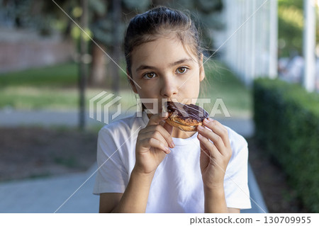 Girl enjoying a chocolate-covered pastry outdoors on a sunny day 130709955