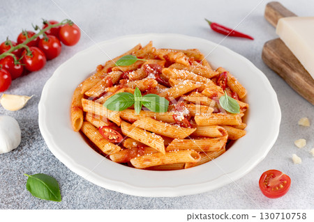 Classic Italian penne pasta with parmesan and tomato sauce on a gray background. Arrabbiata pasta. Classic Italian penne pasta with parmesan and tomato sauce on a gray background. Arrabbiata pasta. 130710758