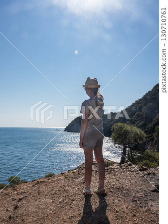 A girl in a hat on a mountain looks at a beautiful panoramic view of the Black Sea 130710761