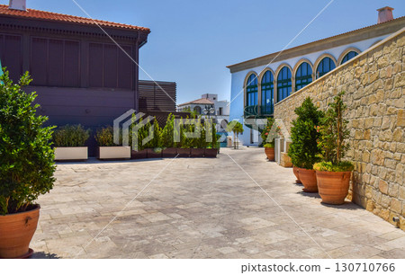 A quiet Mediterranean style courtyard with potted plants, a stone wall and colorful buildings  130710766