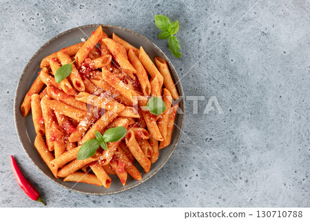 Italian pasta penne arrabiata with tomato sauce and chili pepper on blue background. Top view. Italian pasta penne arrabiata with tomato sauce and chili pepper on blue background. Top view. 130710788