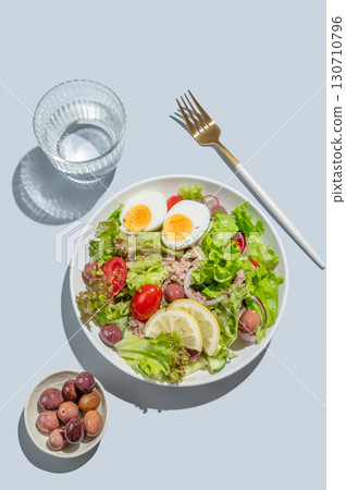 Tuna salad with cherry tomatoes, eggs, olives and cucumbers in a plate on a blue background 130710796
