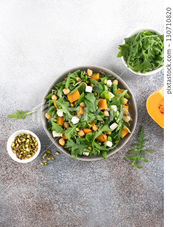 Healthy arugula salad with roasted pumpkin, chickpeas, feta cheese, pistachios on gray background. Top view. 130710820