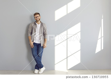 Portrait of confident smiling bearded man standing on grey wall background. 130710955