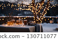 Cozy winter evening: warm beverages and sweet treats on snowy outdoor table with string lights 130711077