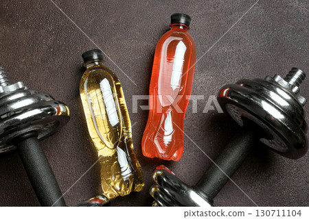 Isotonic sport drink with dumbbells on dark background 130711104