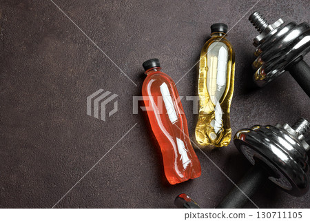 Isotonic sport drink with dumbbells on dark background 130711105