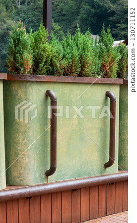 Green planter box with lush evergreen coniferous plants, featuring rustic metal handles and a wooden base, creating a natural and inviting outdoor atmosphere for gardening enthusiasts 130711152
