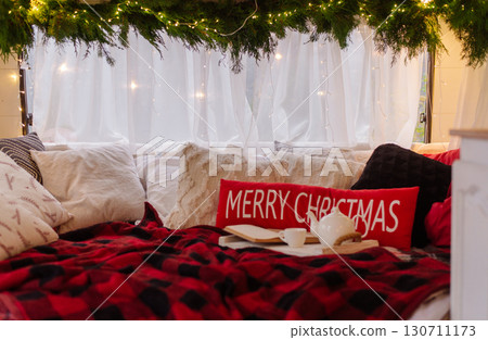 Cozy Christmas interior with pillows, plaid blanket, lights, and festive decor creating holiday warmth. Cozy Christmas interior with pillows, plaid blanket, lights, and festive decor creating holiday warmth. 130711173