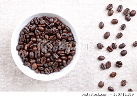 Roasted Arabica coffee beans, in a white bowl, on linen. Dark brown roasted whole seeds of berries from Coffea arabica, also known as Arabian, mountain or Arabica coffee. Close-up, from above. Photo Roasted Arabica coffee beans, in a white bowl, on linen. Dark brown roasted whole seeds of berries from Coffea arabica, also known as Arabian, mountain or Arabica coffee. Close-up, from above. Photo 130711199
