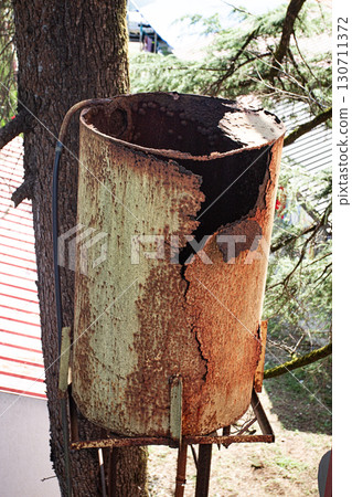 Rusty water tank on a tree stand showcasing decay and weathering in a rural setting Rusty water tank on a tree stand showcasing decay and weathering in a rural setting 130711372