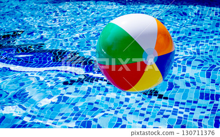 Colorful beach ball floats on the surface of a pool reflecting sunlight on a summer day Colorful beach ball floats on the surface of a pool reflecting sunlight on a summer day 130711376