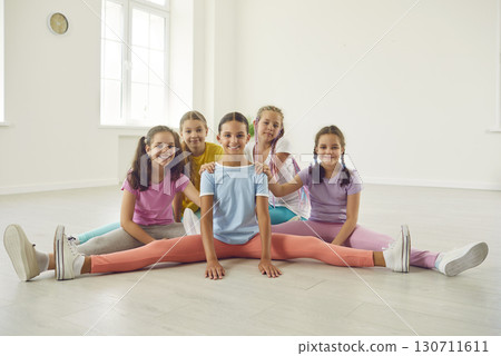 Happy girls sitting on the twine in dance studio and looking cheerful at the camera. Happy girls sitting on the twine in dance studio and looking cheerful at the camera. 130711611