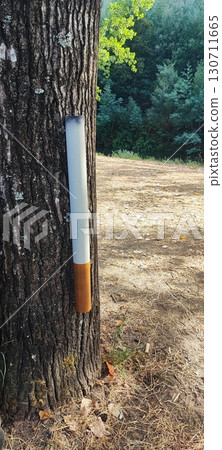 Large cigarette-shaped installation on a tree beside a park trash bin. public art and litter awareness about smoking and pollution Large cigarette-shaped installation on a tree beside a park trash bin. public art and litter awareness about smoking and pollution 130711665