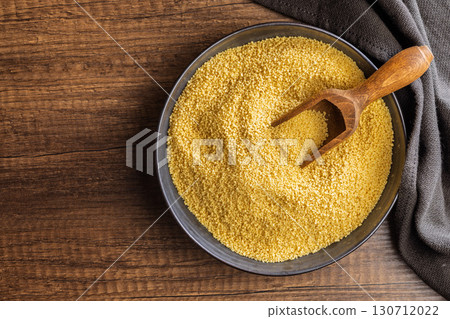 Uncooked couscous in bowl on wooden table. Top view. 130712022