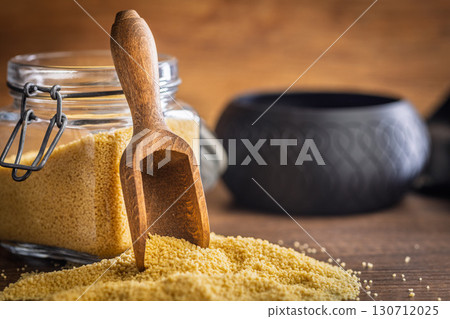 Uncooked couscous and wooden scoop on wooden table. Uncooked couscous and wooden scoop on wooden table. 130712025