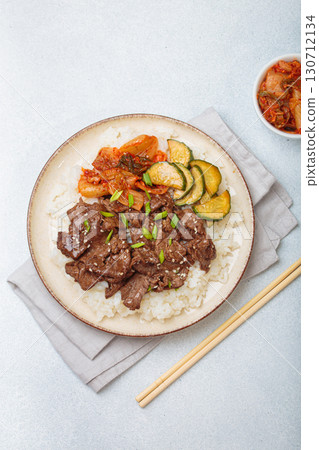 Korean beef bulgogi bowl dish with rice, roasted meat, kimchi and marinated cucumber on white background with chopsticks 130712134