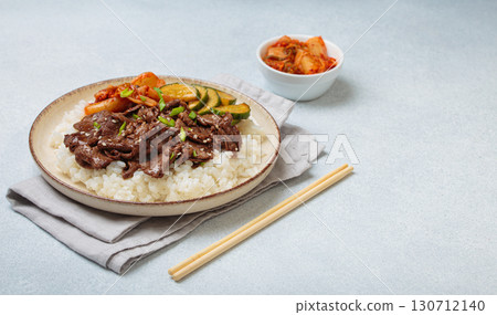 Korean beef bulgogi bowl dish with rice, roasted meat, kimchi and marinated cucumber on white background with chopsticks, space for text Korean beef bulgogi bowl dish with rice, roasted meat, kimchi and marinated cucumber on white background with chopsticks, space for text 130712140