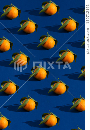 A vibrant, repeating pattern of fresh oranges with green leaves on a bold blue background, casting strong shadows. A vibrant, repeating pattern of fresh oranges with green leaves on a bold blue background, casting strong shadows. 130712161