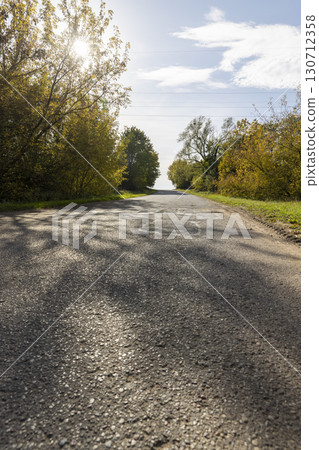 a road in the autumn season, a beautiful bright landscape with a road and yellowing trees in the sunlight a road in the autumn season, a beautiful bright landscape with a road and yellowing trees in the sunlight 130712358